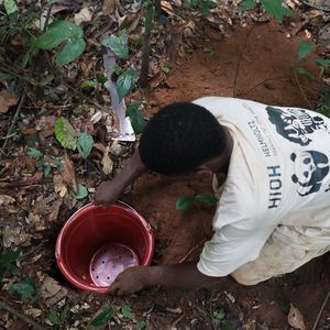 A person is kneeling on the floor in front of a bucket